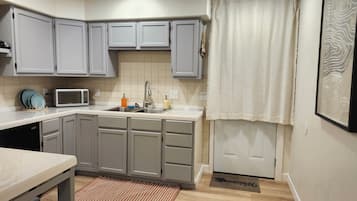 A compact kitchen with grey cabinets, a microwave, a sink, and a wooden floor.