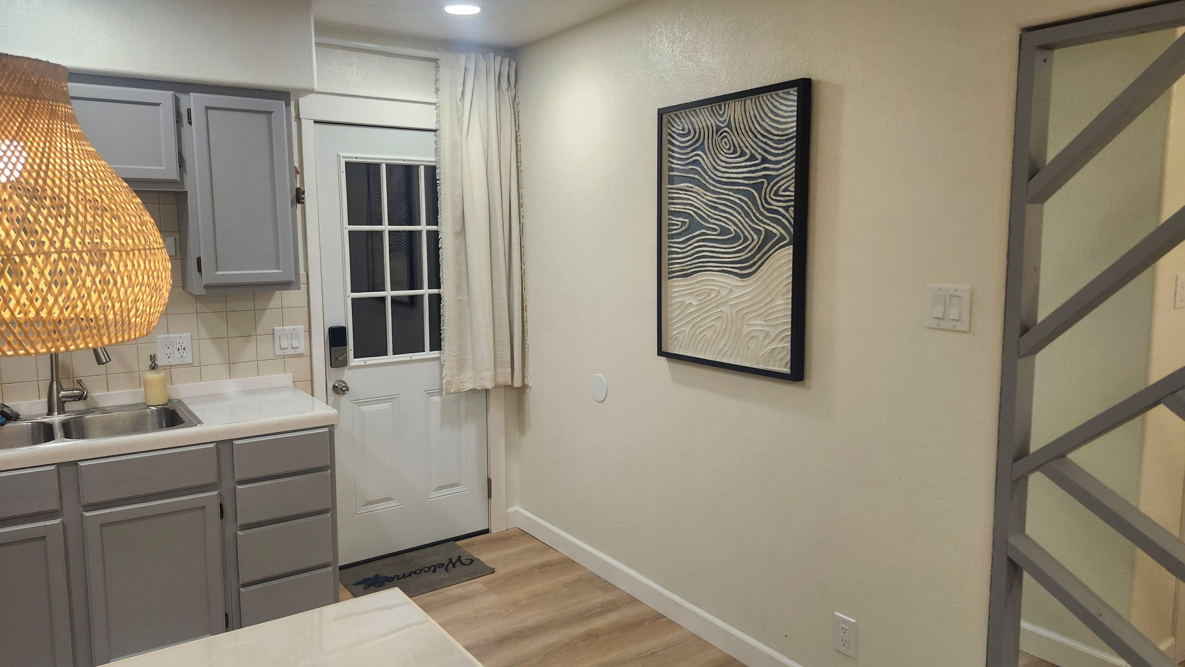 A modern kitchen with grey cabinets, a white countertop, a hanging pendant light, and a door with a window.