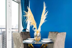 Uma mesa de jantar com um vaso de capim-pampa, uma parede azul e uma janela com cortinas.