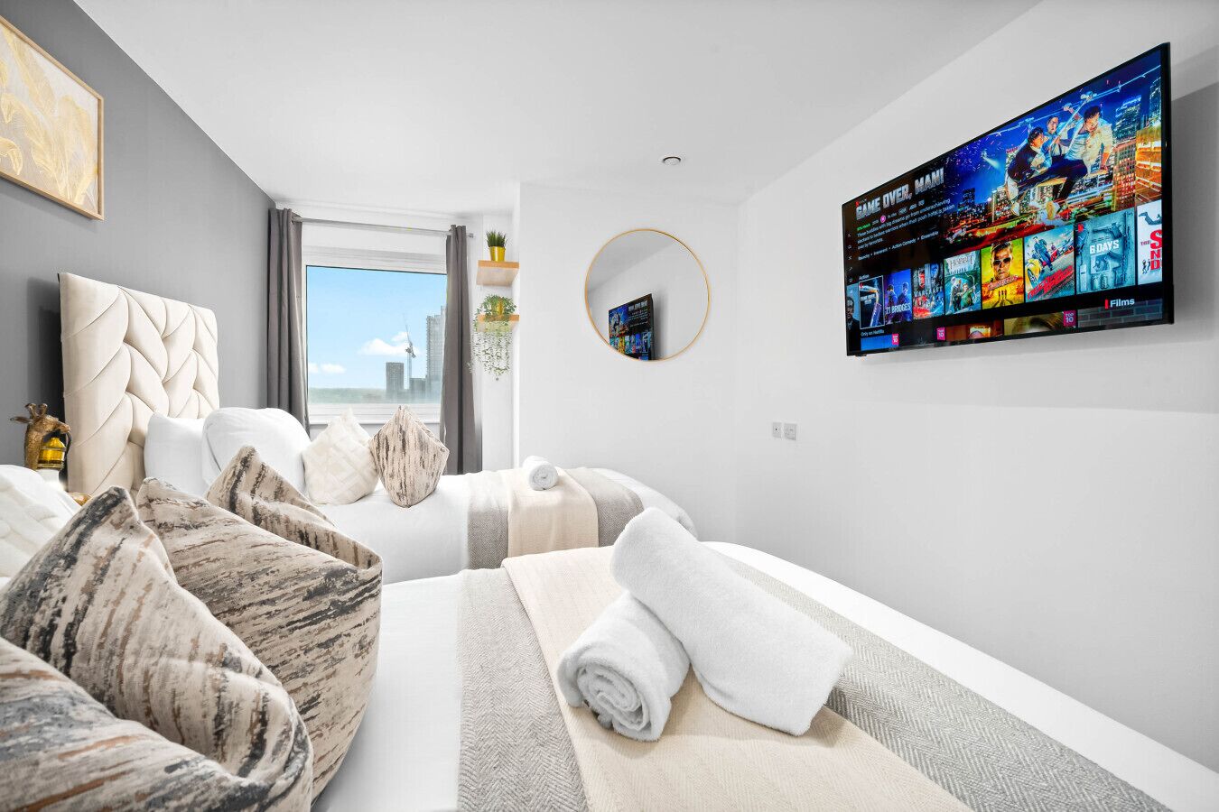 A modern hotel room with a large bed, a TV mounted on the wall, and a view of the city.
