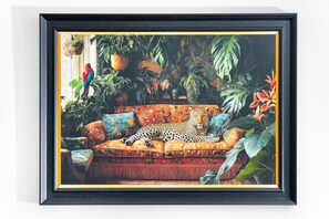 Quadro de um leopardo relaxando em um sofá, rodeado por plantas tropicais exuberantes.
