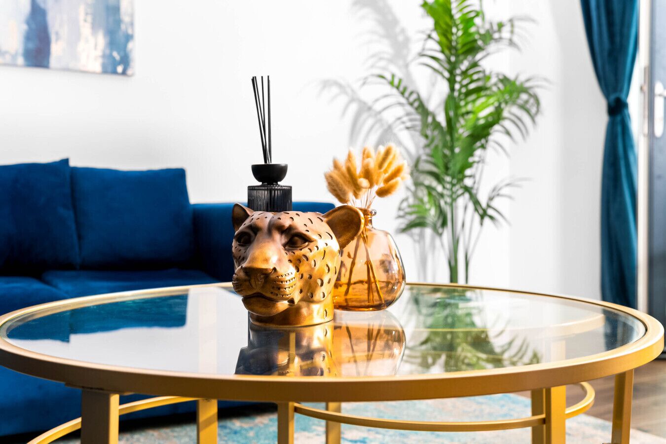 A round glass table with a decorative animal head centerpiece, a blue sofa, and a potted plant in the background.