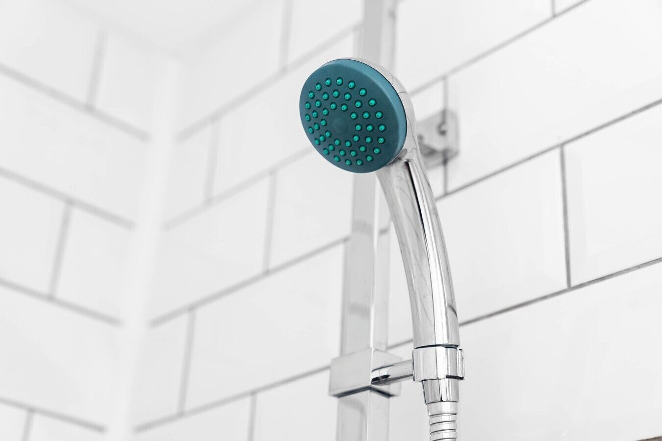 Un pommeau de douche de forme ronde et de couleur bleue, installé sur un mur recouvert de carreaux blancs.