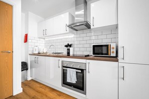 A modern kitchen with white cabinets, a stainless steel oven, a microwave, and a wooden countertop. - Stylish Apartment * Sleep 4 * Parking * Netflix (West Midlands)
