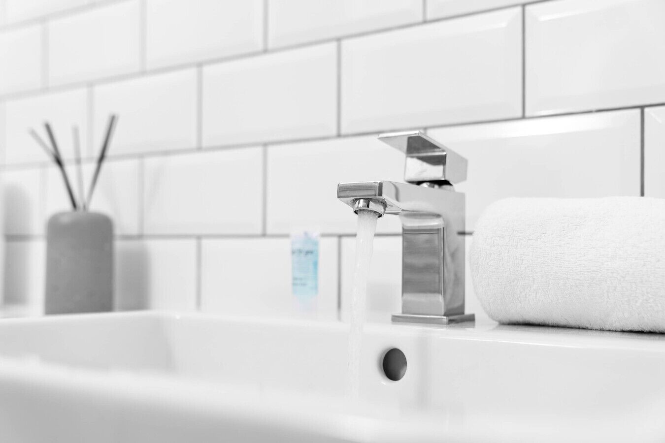 A modern bathroom with a chrome faucet, a white towel, and a soap dispenser.