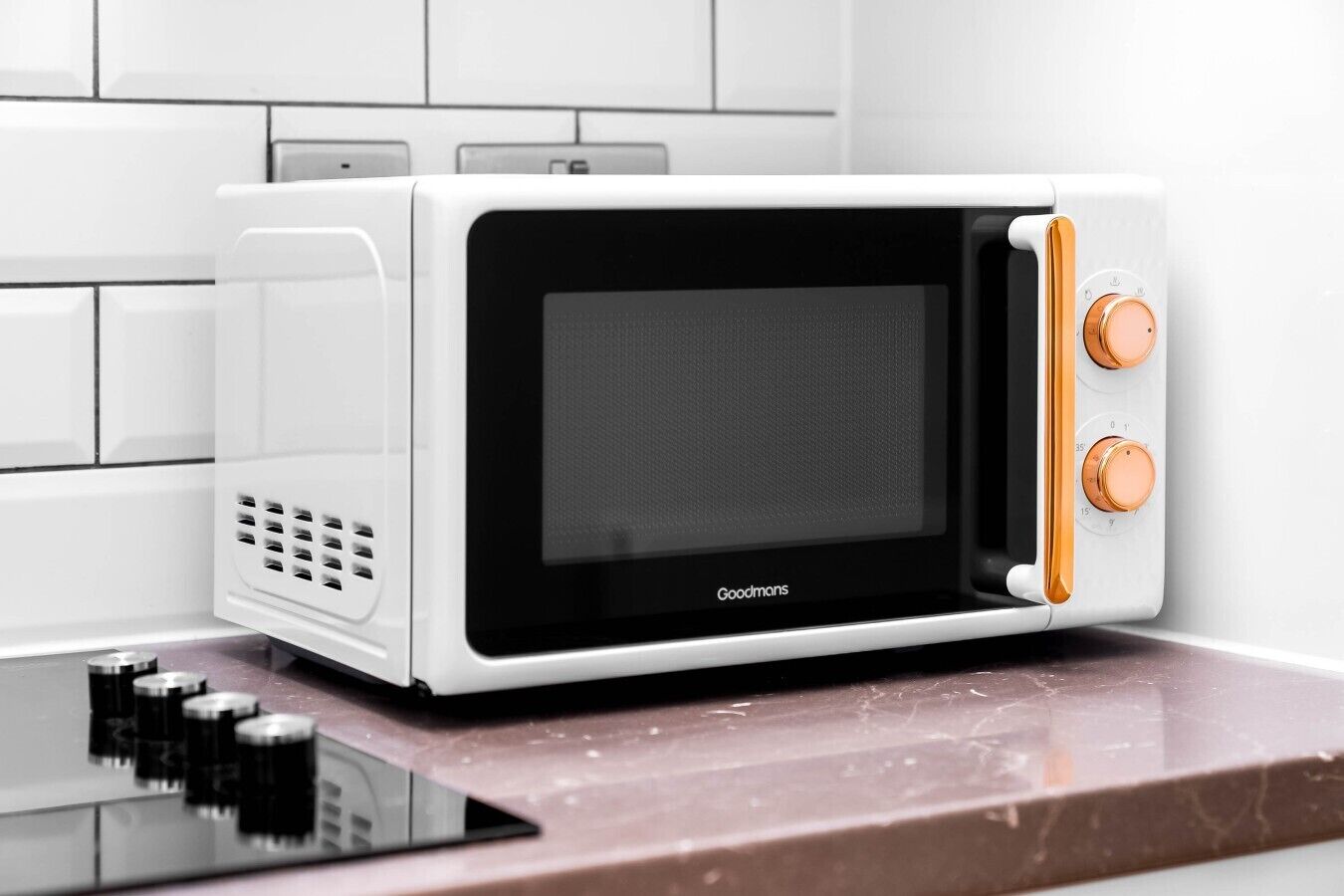 A white microwave oven with a black door and two orange knobs on the right side, placed on a marble countertop.
