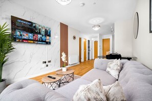 A modern living room with a large flat-screen TV, a grey sofa, a small round coffee table, and a potted plant. - Stylish Apartment * Sleep 4 * Parking * Netflix (West Midlands)