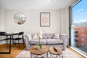 A modern living room with a grey sofa, a dining table with chairs, a round coffee table, a mirror, and a framed artwork on the wall. - Stylish Apartment * Sleep 4 * Parking * Netflix (West Midlands)