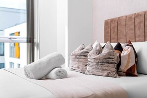 A neatly made bed with a rolled white towel, two textured pillows, and a striped pillow on a white bedspread. - Stylish Apartment * Sleep 4 * Parking * Netflix (West Midlands)