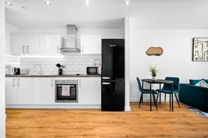 Eine moderne Küche mit weißen Schränken, einem schwarzen Kühlschrank und einem Essbereich mit türkisfarbenen Stühlen und einem schwarzen Tisch.