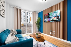 A modern living room with a blue sofa, a wooden coffee table, and a TV mounted on a wooden wall. - Stylish Apartment* Jewellery Q * Parking* Netflix (West Midlands)