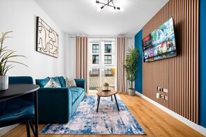 A modern living room with a blue sofa, a coffee table, and a TV mounted on a wooden wall. - Stylish Apartment* Jewellery Q * Parking* Netflix (West Midlands)