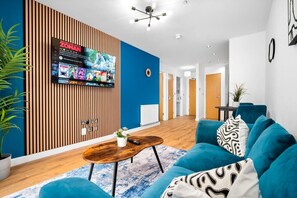 Una sala de estar moderna con un sofá azul, una mesa de centro y un televisor montado en una pared de paneles de madera.