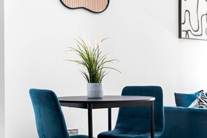A modern room with a round table, two blue chairs, a potted plant, and abstract wall art. - Stylish Apartment* Jewellery Q * Parking* Netflix (West Midlands)