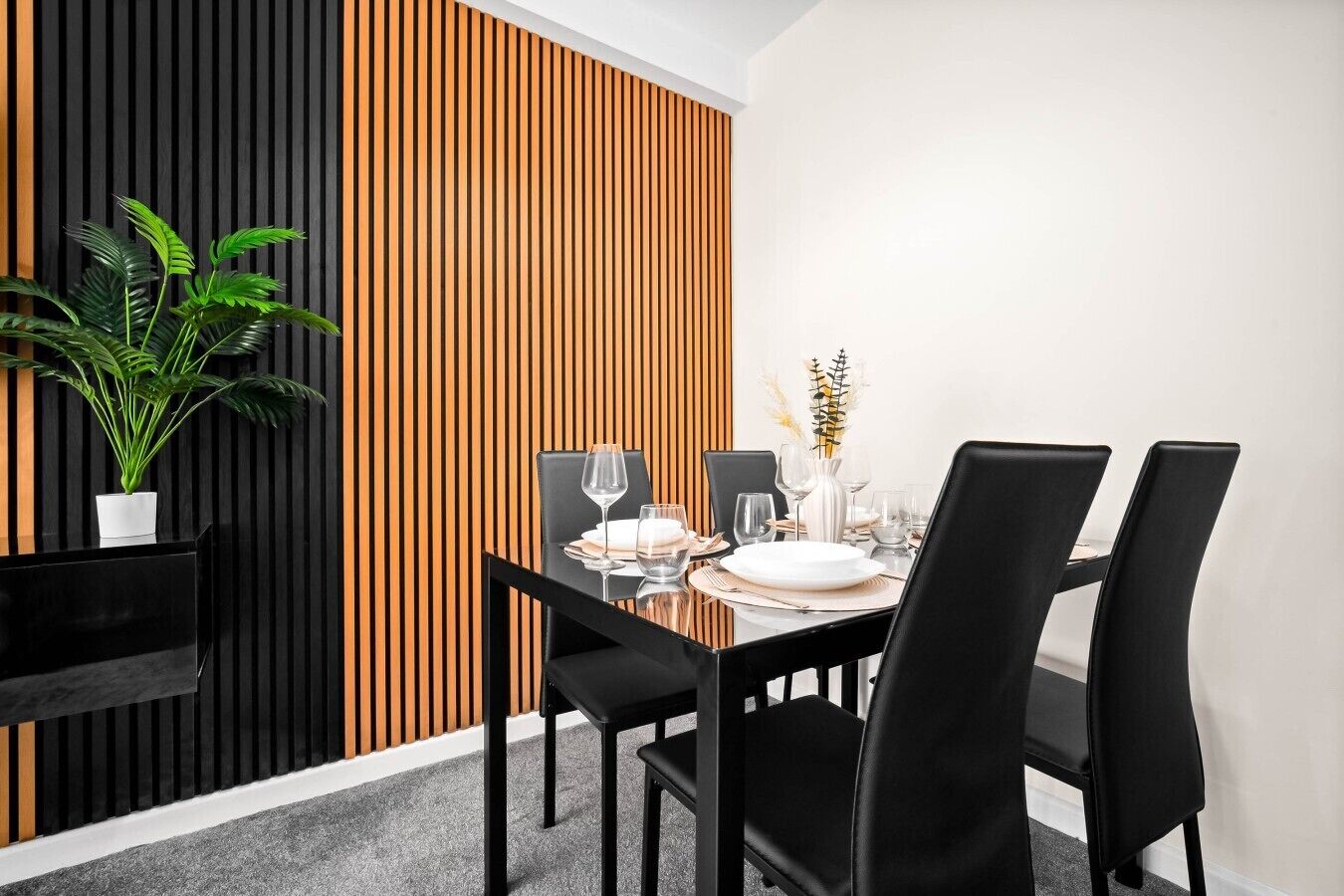 A dining area with a black table, black chairs, and a plant.