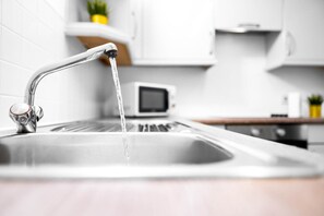 Eine Küchenspüle mit fließendem Wasser, eine Mikrowelle und weiße Schränke.