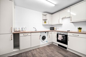 Eine moderne Küche mit weißen Schränken, einer Waschmaschine, einem Backofen und einer Mikrowelle.
