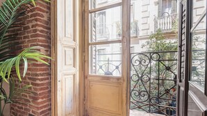 A room with a brick wall, a wooden door, and a window with a wrought iron balcony. - Waou Justicia VI - Short-Term Rental (Madrid)