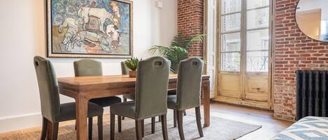 Un coin repas avec une table et des chaises en bois, un grand tableau accroché au mur et une vue à travers une porte vitrée.