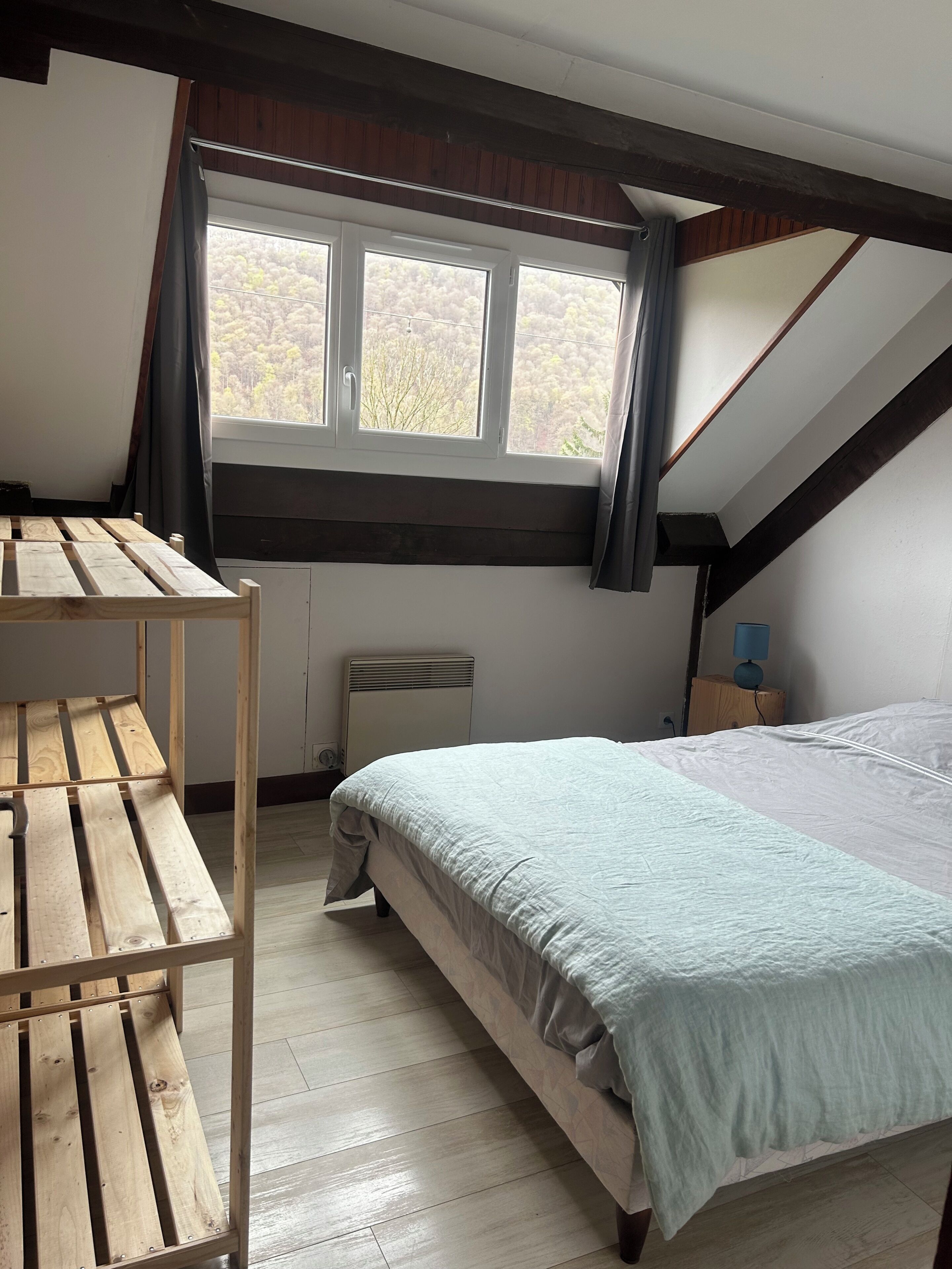 Un dormitorio con techo inclinado, una cama, una mesa de madera y un ventanal con cortinas.