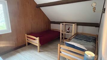 Una habitación pequeña y acogedora con techo inclinado, paredes de madera, una cama individual con un edredón estampado, un estante con un objeto decorativo y una ventana con vistas a la vegetación.