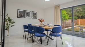 A dining area with a table set for six, surrounded by blue chairs, a skylight above, and a large sliding glass door leading to a garden. - Spacious 5Bed House in Ruislip Sleeps 10 (Ruislip)