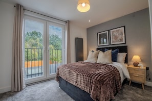A hotel room with a large bed, a nightstand, a lamp, and a view of the outdoors through a sliding door.