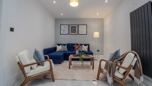 A modern living room with a blue sofa, two wooden chairs, a coffee table, and a floor lamp. - Spacious 5Bed House in Ruislip Sleeps 10 (Ruislip)