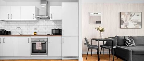 A modern kitchen with white cabinets, a built-in oven, and a dining area with a black sofa and a table.