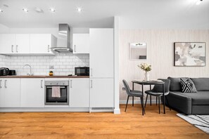 Eine moderne Küche mit weißen Schränken, einem eingebauten Ofen und einem Essbereich mit einer schwarzen Couch und einem Tisch.