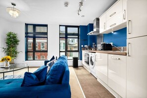 A modern living room with a blue sofa, a glass coffee table, and a view of the city through large windows. - Luxury 2 Bed Apartment - Parking - JQ - City Centre - Bedroom TV (West Midlands)