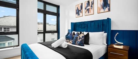A modern bedroom with a large bed, a nightstand, and a window with blinds.