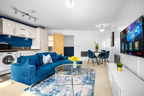 Ein modernes Wohnzimmer mit einem blauen Sofa, einem Glastisch und einem Essbereich mit blauen Stühlen.