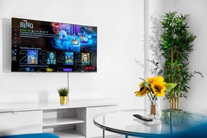 Ein modernes Wohnzimmer mit Flachbildfernseher an der Wand, einem Glastisch, einer Topfpflanze und einer Vase mit Blumen.