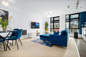 Ein modernes Wohnzimmer mit einer Couch, Sesseln, einem Fernseher und einem Essbereich mit Tisch und Stühlen.