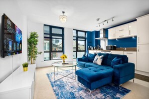 Ein modernes Wohnzimmer mit einem blauen Sofa, einem Glastisch und einem an der Wand befestigten Flachbildfernseher.