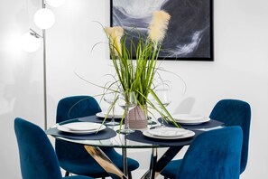 A dining table with a glass top, surrounded by blue chairs, and a vase with green plants and pampas grass. - Luxury 2 Bed Apartment - Parking - JQ - City Centre - Bedroom TV (West Midlands)