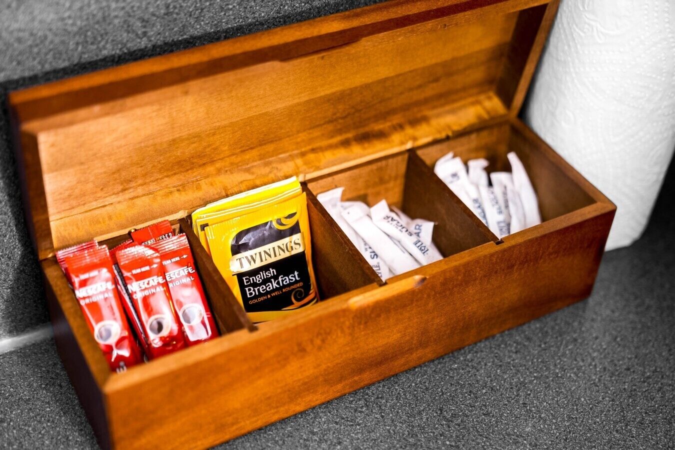 A wooden box containing various food items including Twinings English Breakfast tea and Nestle Original coffee.