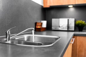 Une cuisine moderne dotée d’un évier en acier inoxydable, d’un meuble en bois et d’un dosseret en marbre.