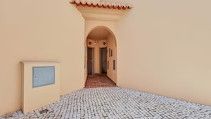 A corridor with a tiled floor leading to a door, a wall-mounted electrical box, and a tiled roof. - Baia da Luz Resort | 2BR with Pool by LovelyStay (Praia da Luz)