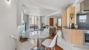 Eine moderne Wohnung mit einem Glastisch, weißen Stühlen, einer Küche mit Holzschränken und einem Wohnbereich mit Sofa und Fernseher.