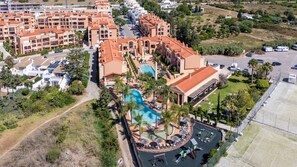 Vista aérea de um resort com vários edifícios, uma piscina e estacionamento.