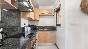 Uma cozinha compacta com bancada de granito, armários de madeira, forno embutido e uma janela com persianas.