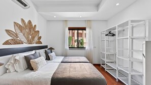 A hotel room with a bed, a wardrobe, a wall art piece, and a window with a view of greenery. - Baia da Luz Resort | 1BR with Pool by LovelyStay (Praia da Luz)