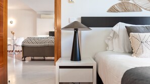 Ein modernes Schlafzimmer mit Bett, Nachttisch, Lampe und Blick auf einen Essbereich.