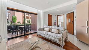 Ein modernes Wohnzimmer mit einer Couch, einem Glastisch und Blick auf eine Terrasse.