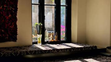 Una habitación con un ventanal grande, una alfombra estampada, una mesita y un adorno en el alféizar.