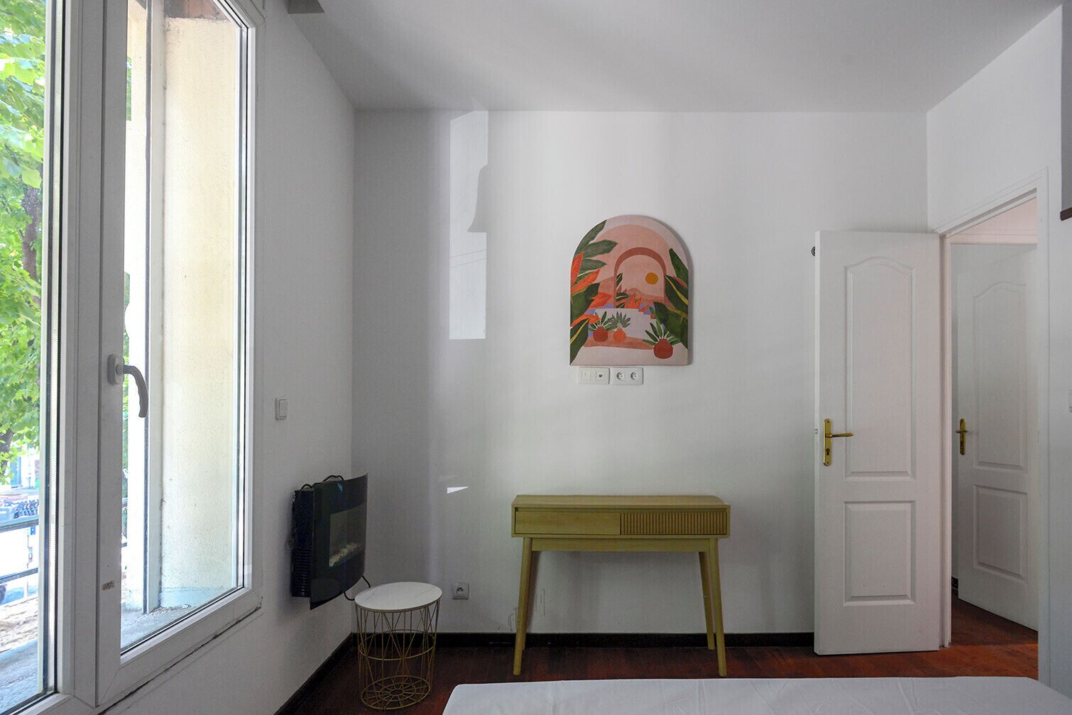 A room with a bed, a small round table, a wall-mounted TV, and a door.