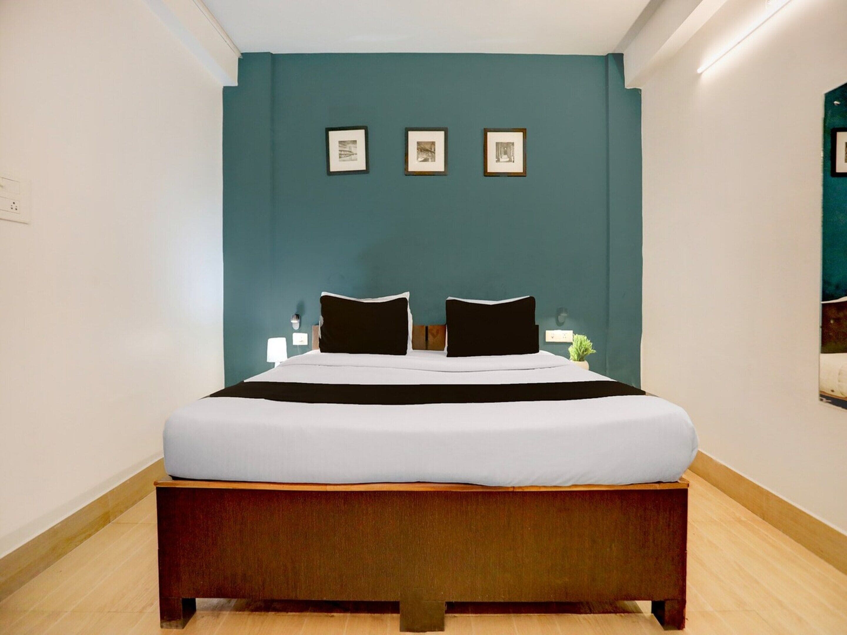 A hotel room with a bed, a teal accent wall, and three framed pictures.