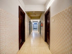 A long, narrow hallway with tiled walls and wooden doors, leading to a room with a window and a curtain.